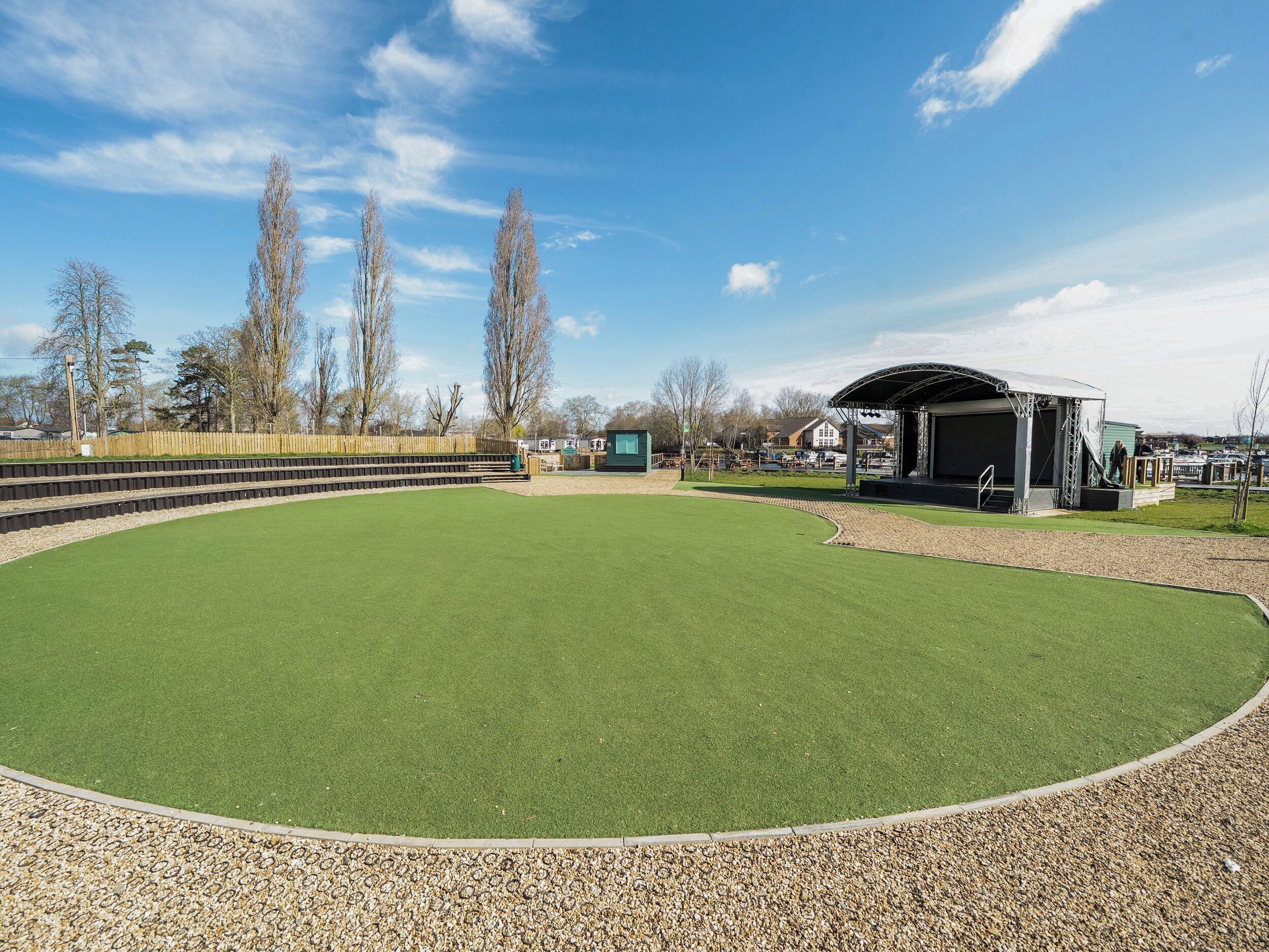 A golf course with a putting green, a spectator area, and a covered pavilion.