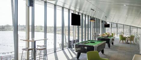 A pool table and chairs in a room with large windows overlooking a body of water.