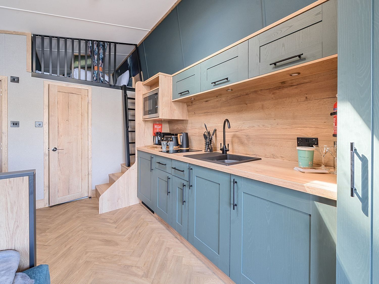 A modern kitchen with light blue cabinets, a wooden countertop, and a black sink.