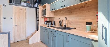 A modern kitchen with light blue cabinets, a wooden countertop, and a black sink.