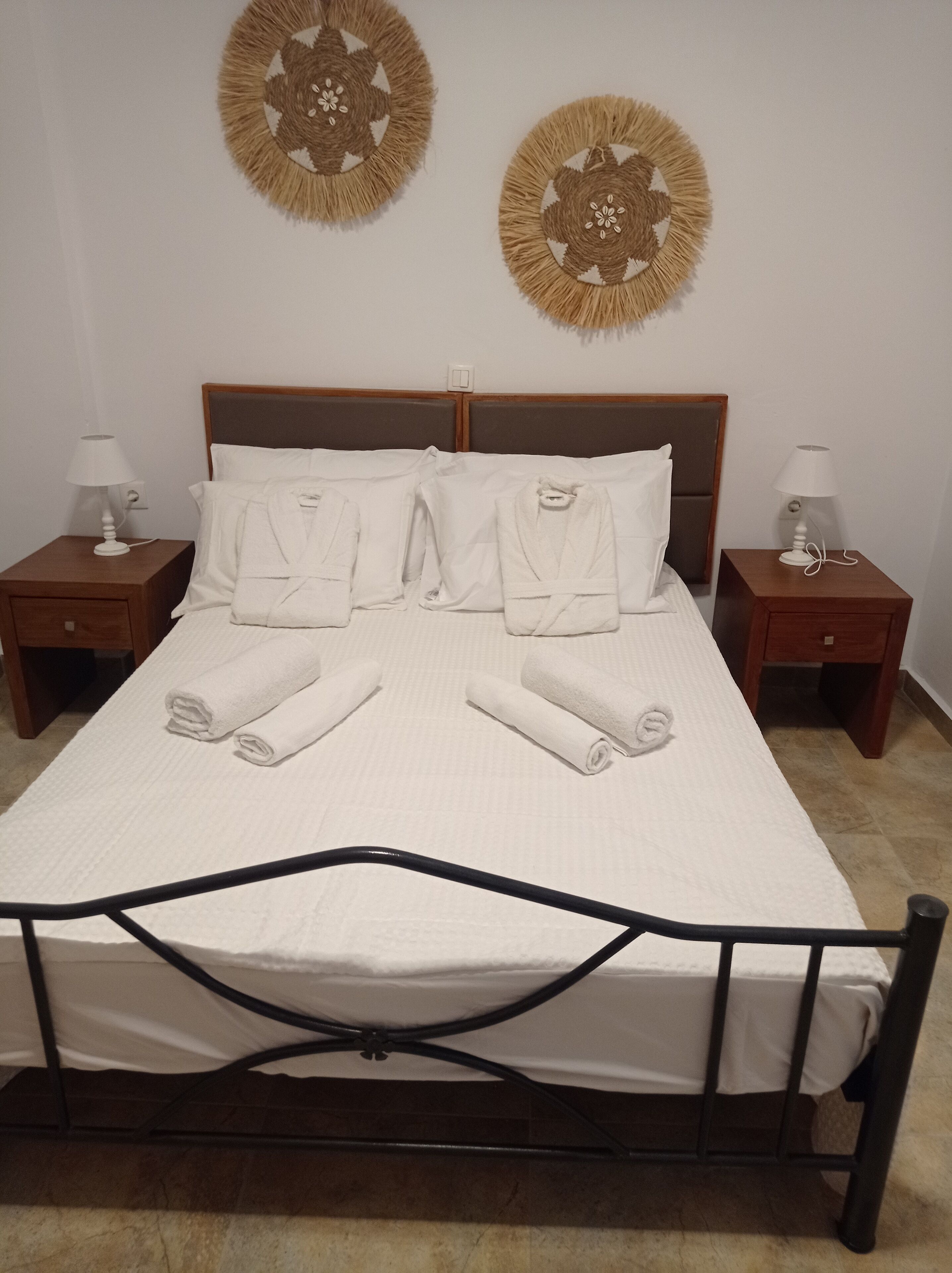 Un lit bien fait, avec du linge de lit blanc et des serviettes pliées, deux tables de chevet avec des lampes et deux éléments de décoration murale.