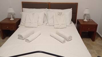 Un lit bien fait, avec du linge de lit blanc et des serviettes pliées, deux tables de chevet avec des lampes et deux éléments de décoration murale.