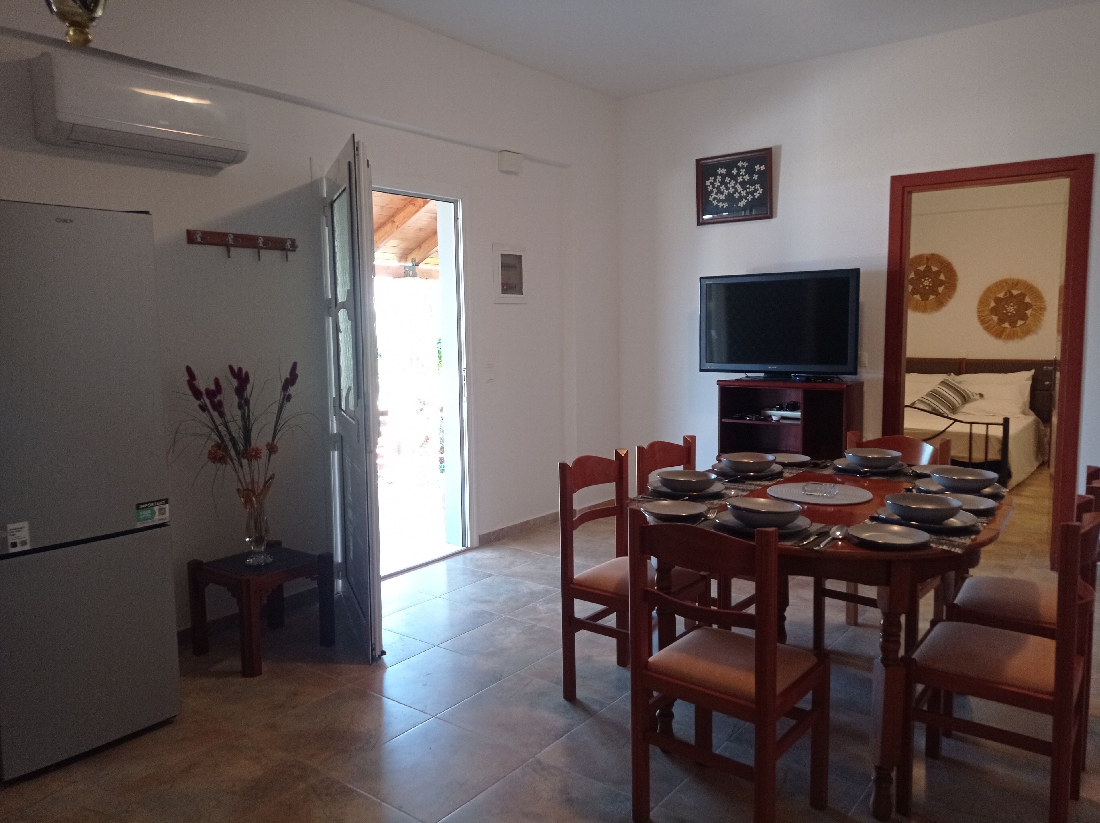 Un coin repas avec une table dressée pour quatre personnes, un téléviseur posé sur un meuble, et un lit en arrière-plan.