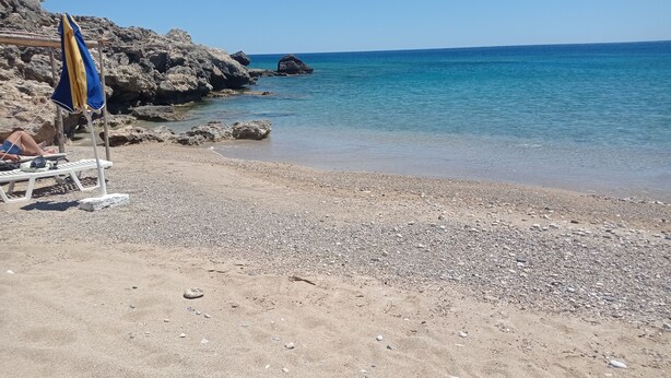 Une plage de galets, avec un promontoire rocheux et une mer d’un bleu limpide.