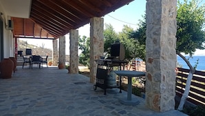 Un espace extérieur abrité, doté de piliers en pierre, d’un barbecue et offrant une vue sur la mer.