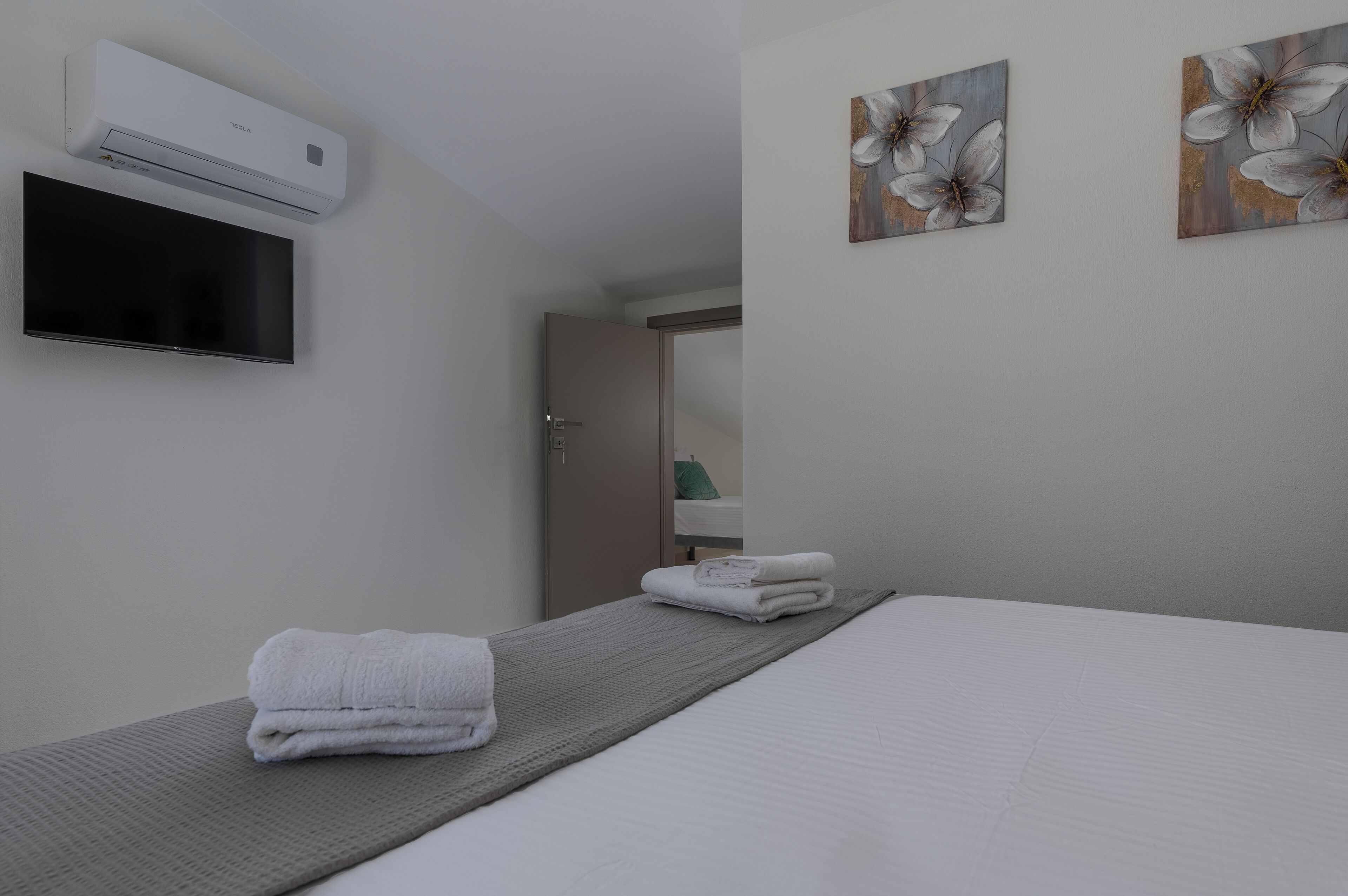 A hotel room with a bed, a flat-screen TV mounted on the wall, and two paintings on the wall.
