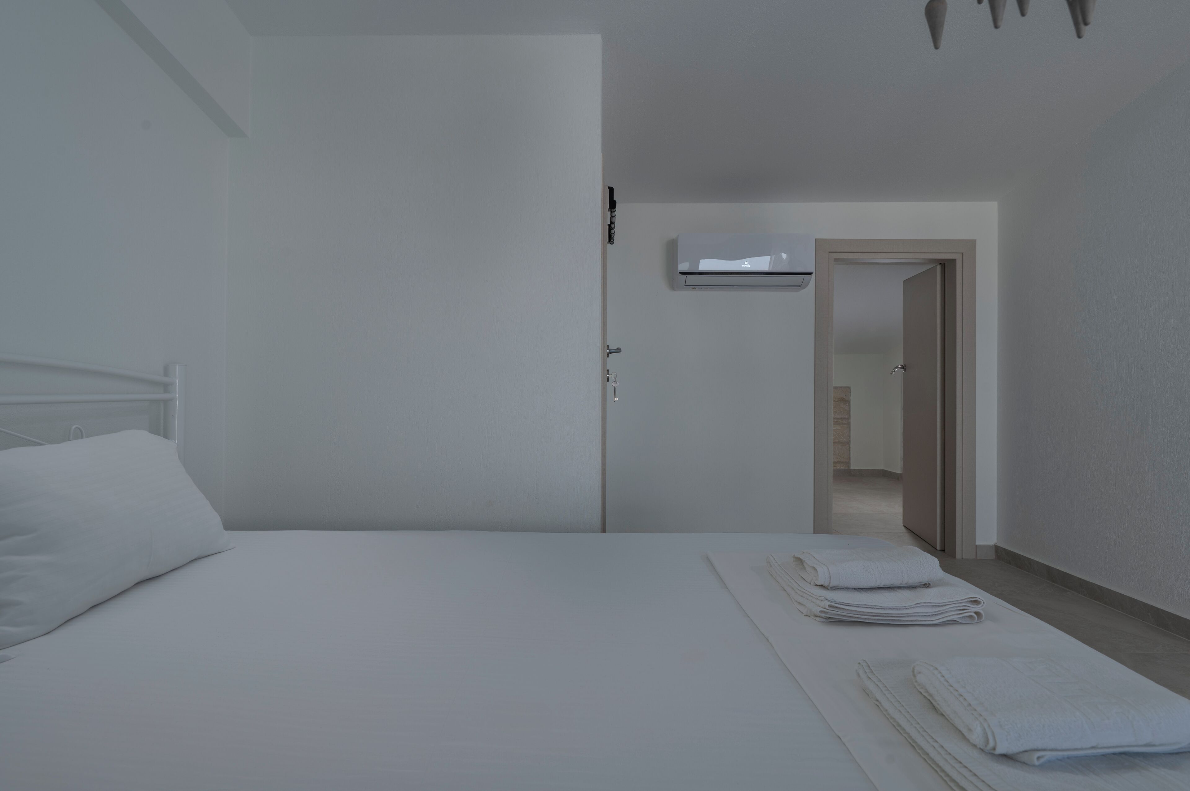 A minimalist hotel room with a bed, a door, and a wall-mounted air conditioning unit.