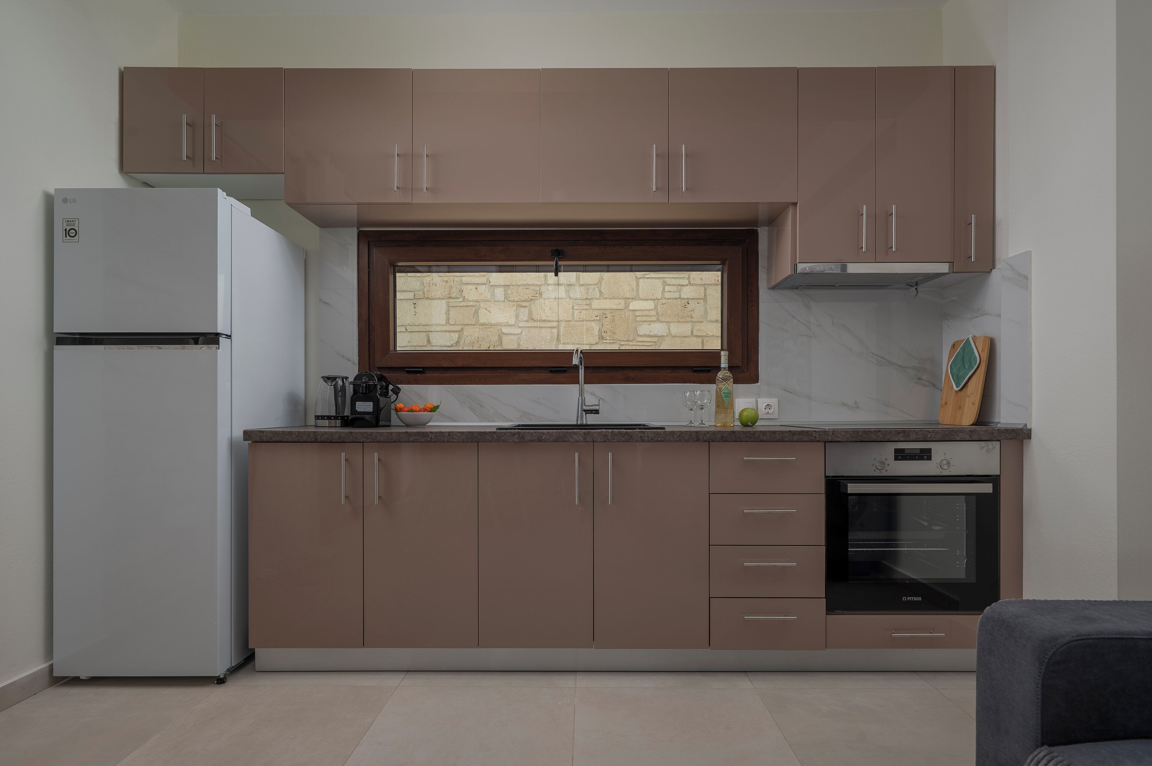 A modern kitchen with brown cabinets, a white refrigerator, a built-in oven, and a stone backsplash.