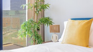 A hotel room with a bed, a lamp, a large window, and a potted plant.