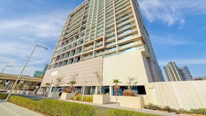 A modern high-rise building with a grid of balconies, a flat facade, and a clear sky.