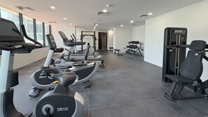 A modern gym with various cardio machines, weightlifting equipment, and a bench.