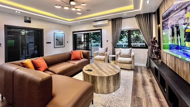 Ein modernes Wohnzimmer mit einem braunen Ledersofa, zwei Sesseln, einem Holztisch und einem flachbildfernseher an der Wand.