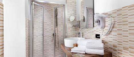 Un baño moderno con ducha envuelta en cristal, un lavamanos blanco y un mueble de tocador de madera.