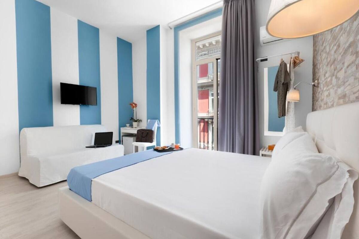 A hotel room with two beds, a desk, a TV, and a balcony with curtains.
