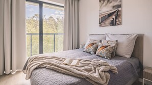 A bedroom with a large window, a bed with a quilted bedspread, multiple pillows, and a book on the bed. - Horizonte Rogowo Klimatyzacja Blisko pla y i Jeziora (Trzebiatow)