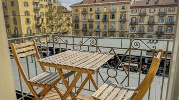 Un balcone con tavolo e due sedie in legno, affaccia su una vista urbana con edifici a più piani.