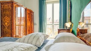 A hotel room with two beds, a wooden wardrobe, and a view of the city through a large window. - Antique Heritage Suite in Porta Nuova (Torino)