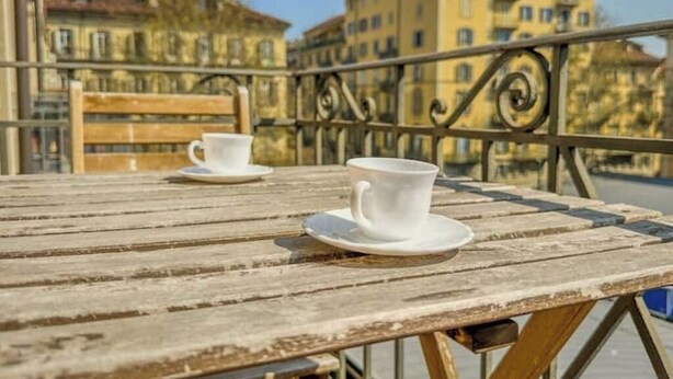 A wooden table with two white cups on a balcony overlooking buildings. - Antique Heritage Suite in Porta Nuova (Torino)