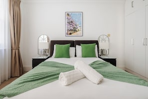 A neatly arranged hotel room with a bed, two bedside tables, a mirror, a framed picture on the wall, and a wardrobe.