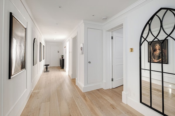 A hallway with framed artwork on the walls, a potted plant, and a door with a black metal frame.