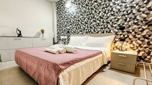 A neatly made bed with a pink blanket and white linens, a bedside table with a lamp, and a wall with a geometric pattern. - Loft Design + Garage and Fitness Area (Torino)