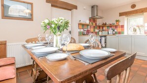 A dining area with a wooden table set for four, a vase of flowers, and a loaf of bread.