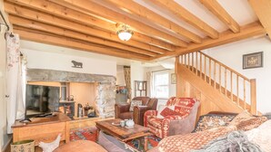 A cozy living room with a fireplace, wooden beams, a sofa, a coffee table, and a staircase.