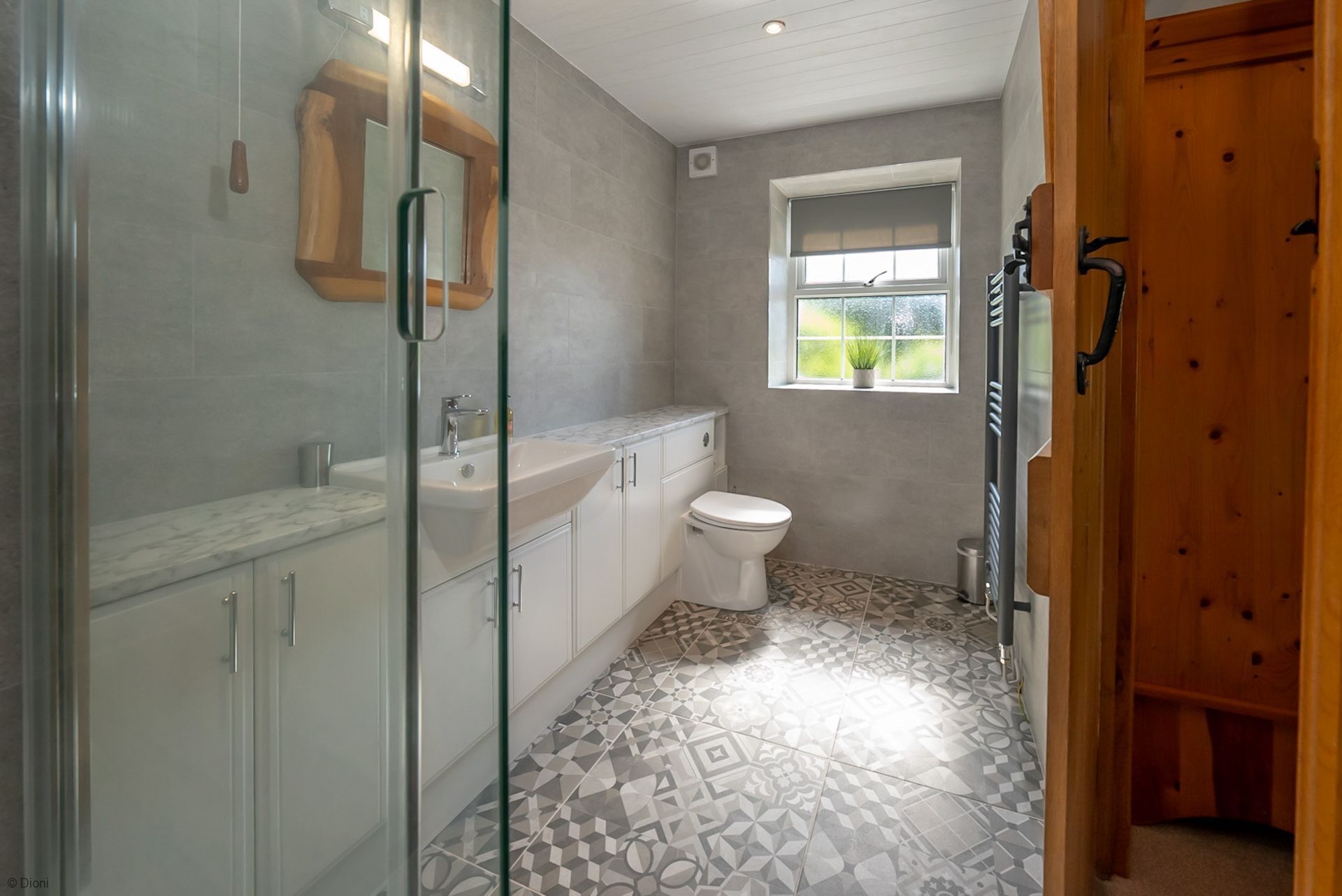 A bathroom with a shower, sink, toilet, and a window with a view of greenery.
