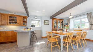 Una cocina con armarios de madera, una isla central con taburetes y una mesa de comedor preparada para seis personas.