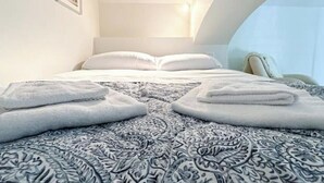 A bedroom with a patterned bedspread, neatly folded towels, and a framed picture on the wall.