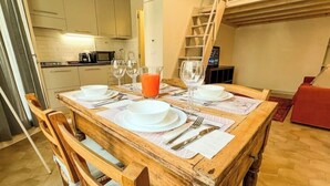 A wooden dining table set with white plates, glasses, and cutlery, with a red beverage on the table.