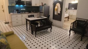 A compact kitchen with white cabinets, a microwave, and a refrigerator. There is a dining table with chairs and a bench. The floor has a black and white checkered pattern. - Cozy 1BR Apt in Siolim 3km to Uddo Beach (Siolim)