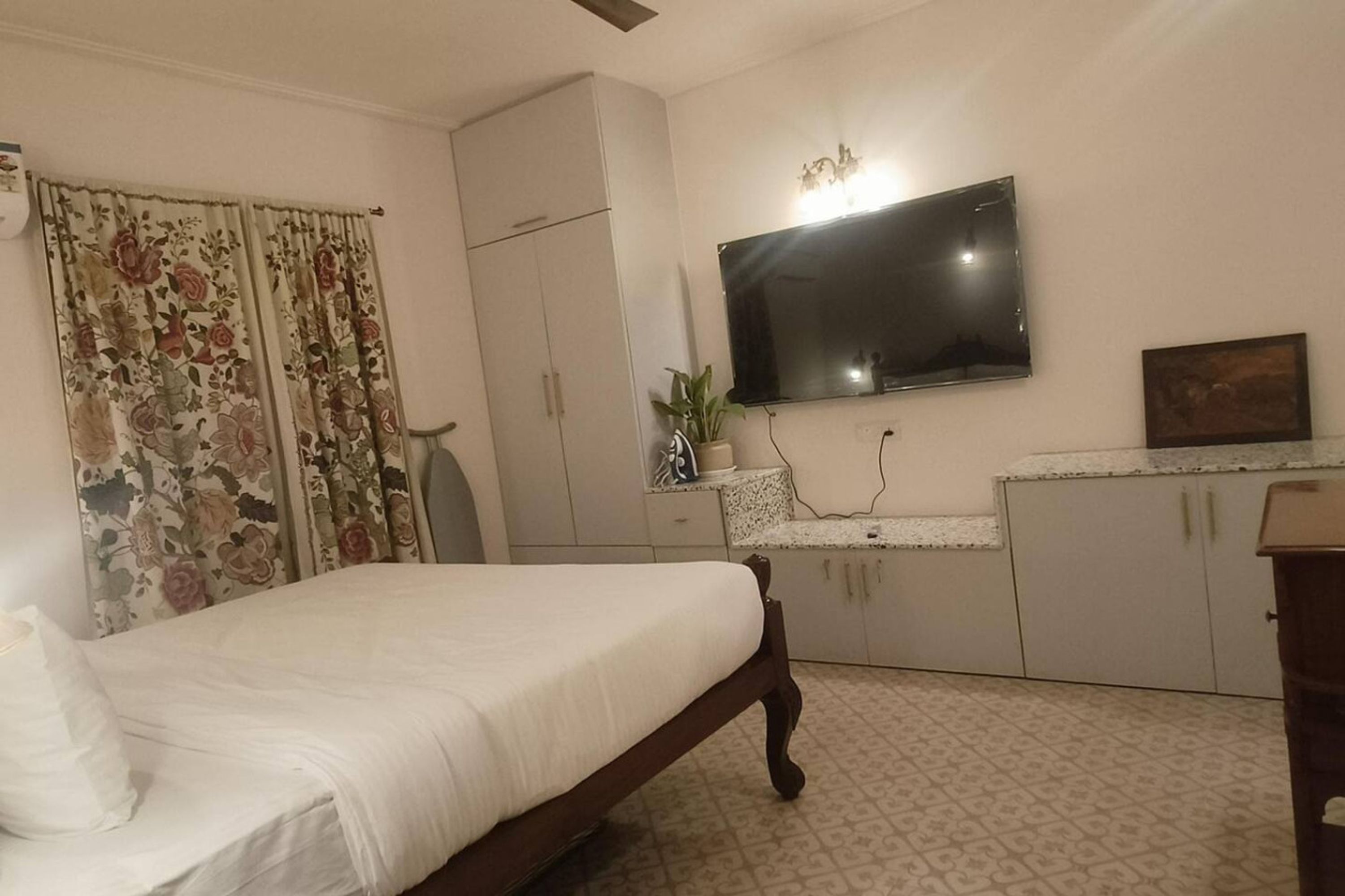 Une chambre à coucher avec un lit, un téléviseur fixé au mur, une armoire et une petite table sur laquelle est posée une plante.