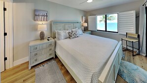 Un dormitorio con cama, mesitas de noche, ventilador de techo, ventana con vistas y una puerta.