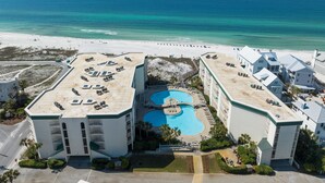 Luftaufnahme eines Resorts mit einem zentralen Swimmingpool, Strandvillen und einem Sandstrand.