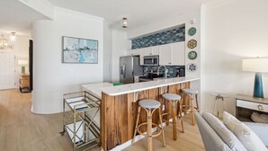 Eine moderne Küche mit weißen Schränken, einer Marmorarbeitsplatte und einer eingebauten Mikrowelle. An der Bar stehen drei Hocker, und eine Holzwand sorgt für Wärme.