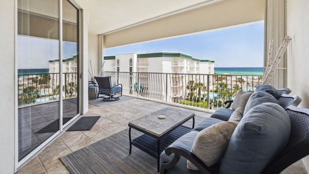 Ein Balkon mit Blick auf den Strand, eine Couch, ein Sessel und ein Tisch.
