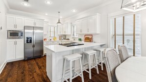 Una cocina moderna con armarios blancos, un refrigerador de acero inoxidable, microondas integrado y una isla central con taburetes de bar.
