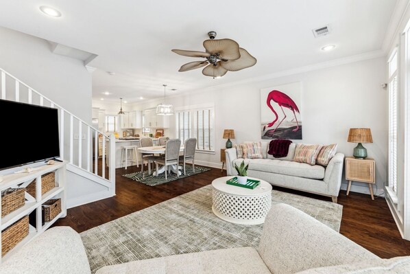 A spacious living room with a television, a dining area, and a ceiling fan. - Beach House Near Parks and Pool (Panama City Beach)