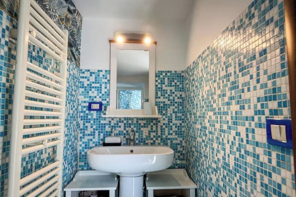 A bathroom with a white sink, a mirror, and blue mosaic tiles on the walls.