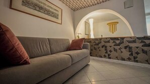 A living room with a sofa, a framed picture on the wall, and a patterned wall behind a semi-circular archway. - Royal Palace Suite in Piazza Castello (Torino)