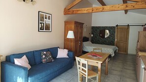 A cozy room with a blue sofa, wooden ceiling beams, a wooden table, and a bed with a floral bedspread. - Large studio with outdoor jacuzzi  (Lagnes)