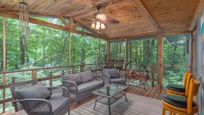 A wooden deck with wicker furniture, a ceiling fan, and a view of the forest.