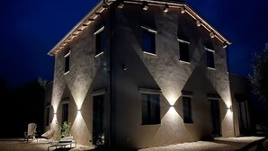Ein mehrstöckiges Gebäude mit einer einzigartigen, geometrischen Fassade, beleuchteten Fenstern und Außenbestuhlung.