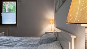 Un dormitori amb un llit, una finestra amb persianes, una làmpada i una obra d'art penjada a la paret.