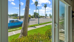 A view from inside a room looking out to a street with palm trees, a blue car, and a clear sky. - Beautiful 2 Bed Beach Condo #104 2 Bedroom Condo by RedAwning (Carpinteria)