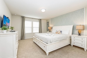 A bedroom with a bed, bedside tables, a dresser, a window with curtains, and a wall with a patterned wallpaper.