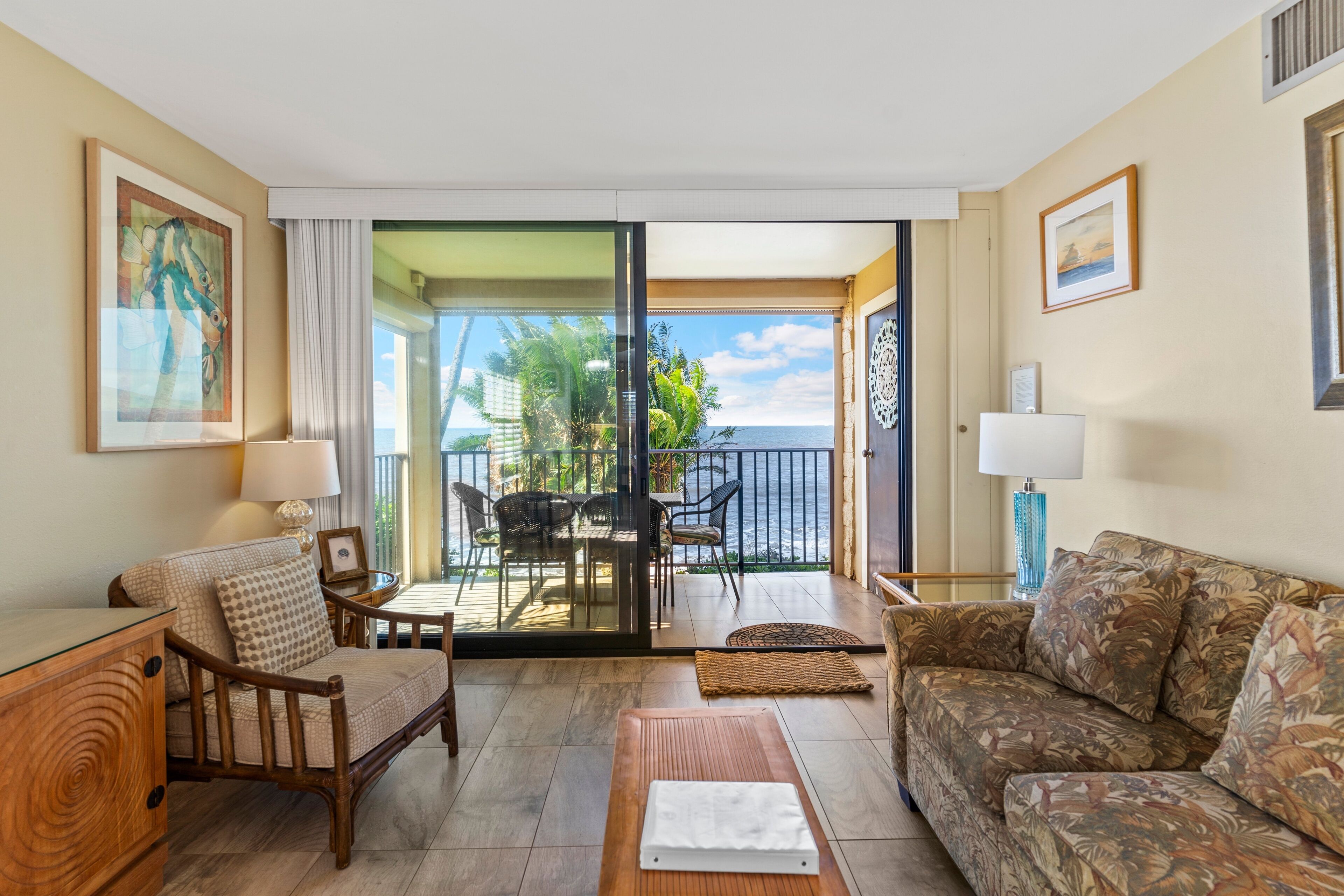 A room with a sofa, a chair, a table, and a balcony with a view of the sea.