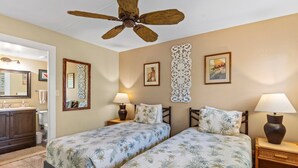 A hotel room with two beds, a ceiling fan, a bathroom with a mirror, and decorative wall art.