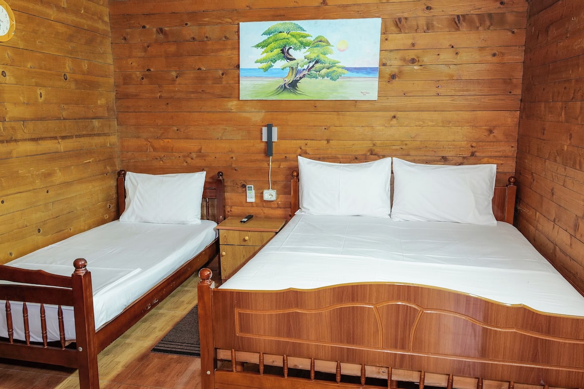 A wooden cabin room with two beds, a painting of a tree, and a clock on the wall.